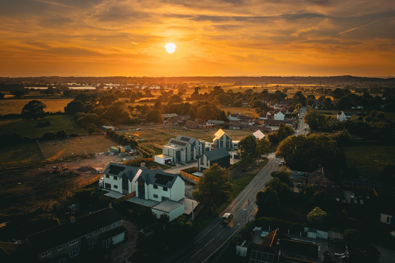 An aerial shot of a property development site in Rangeworthy, South Gloucestershire during golden hour in June 2025 facing towards the orange sun.