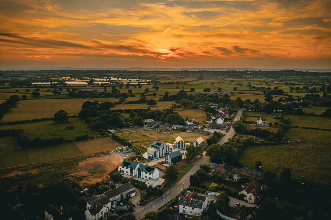 An aerial shot of a property development site in Rangeworthy, South Gloucestershire during golden hour in June 2025 facing towards the orange sun.