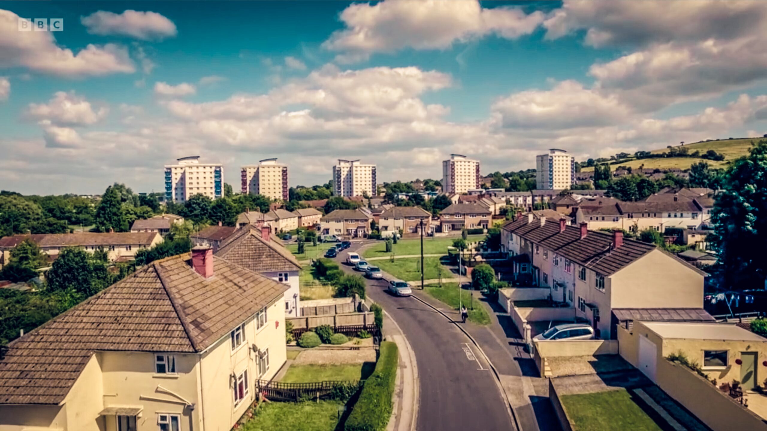 Three Girls - BBC ONE - Scene An aerial shot of a road in a council estate in Hartcliffee, Bristol following a talent as she's walking up the street.