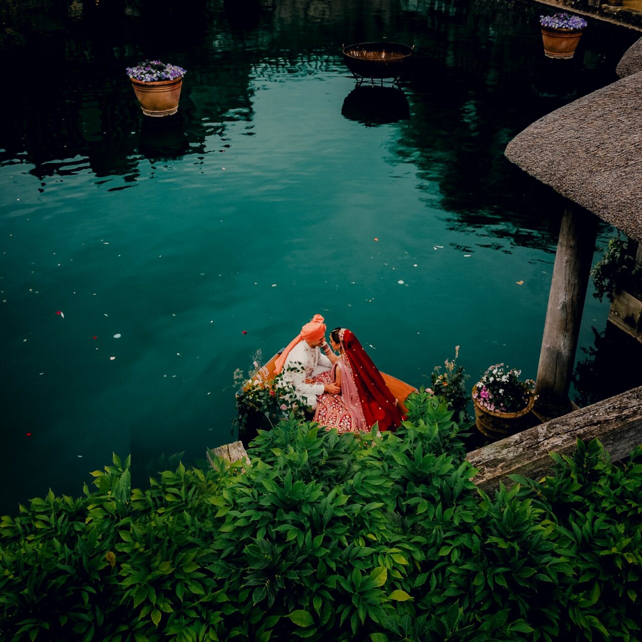 An aerial shot of the bride and groom in a row boat on the lake at Euridge Manor near the dock looking into each others eyes.