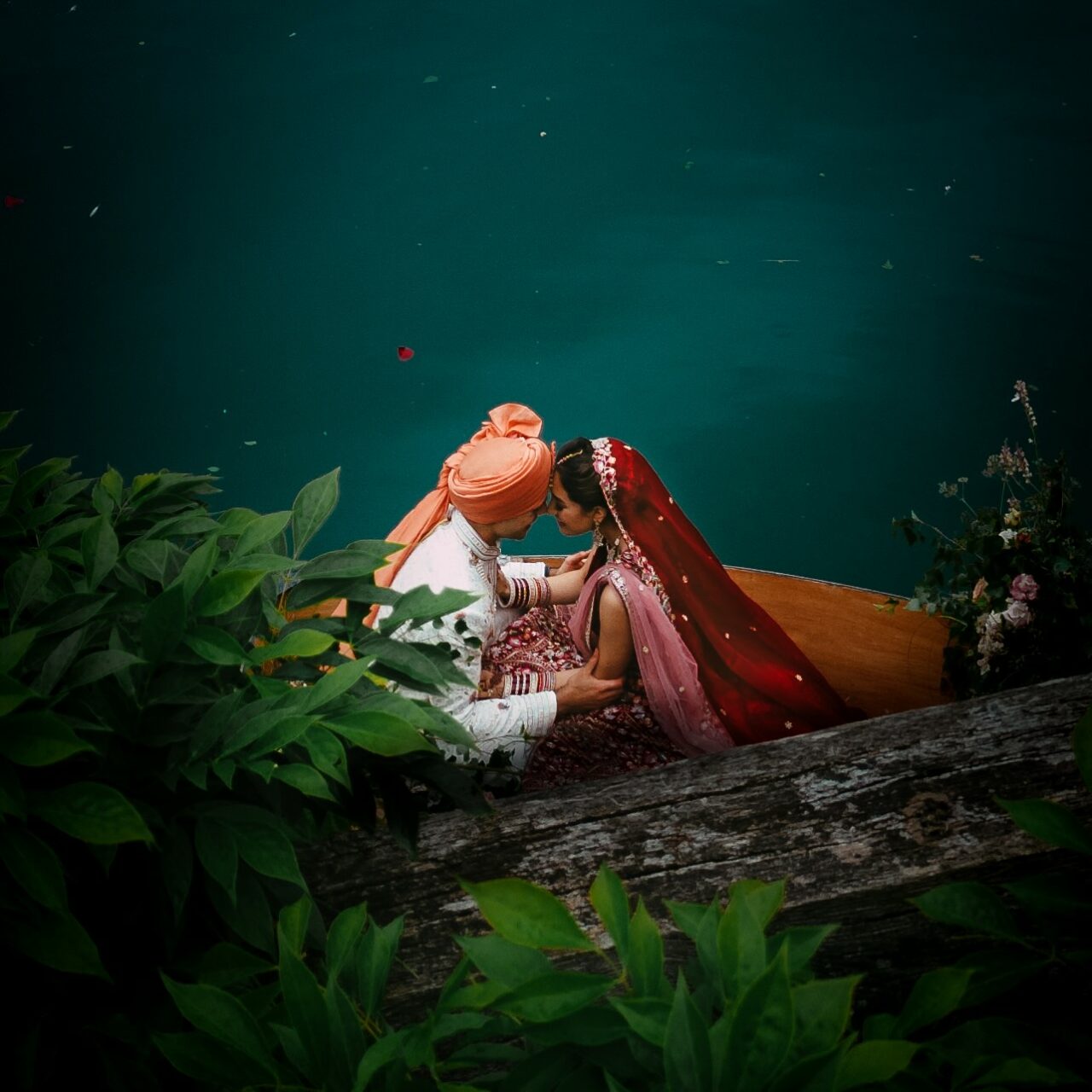 An aerial shot of the bride and groom in a row boat on the lake at Euridge Manor near the dock looking into each others eyes with their noses touching.